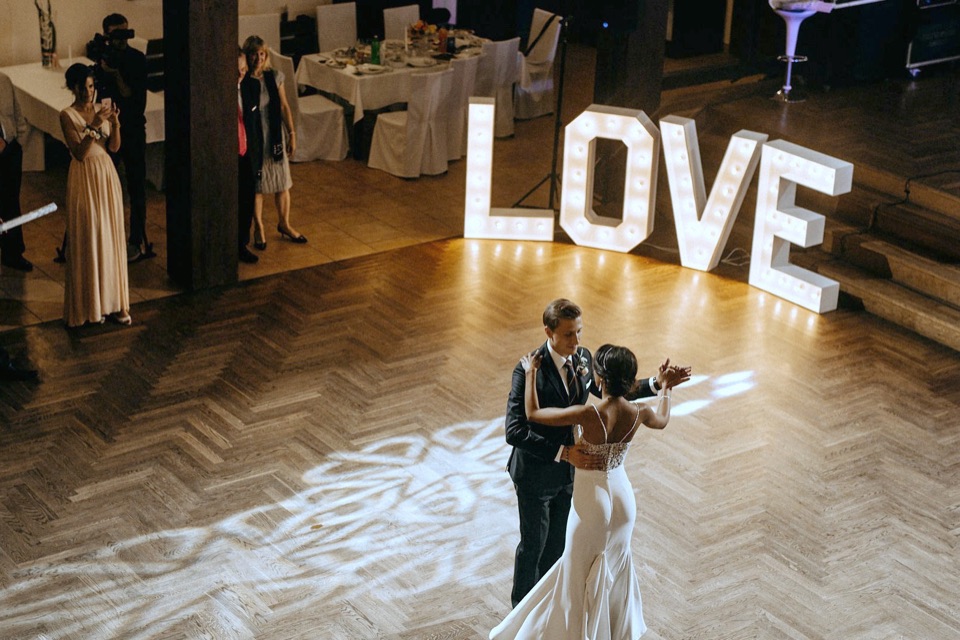 Para młoda tańczy pierwszy taniec na parkiecie przed podświetlanym napisem LOVE